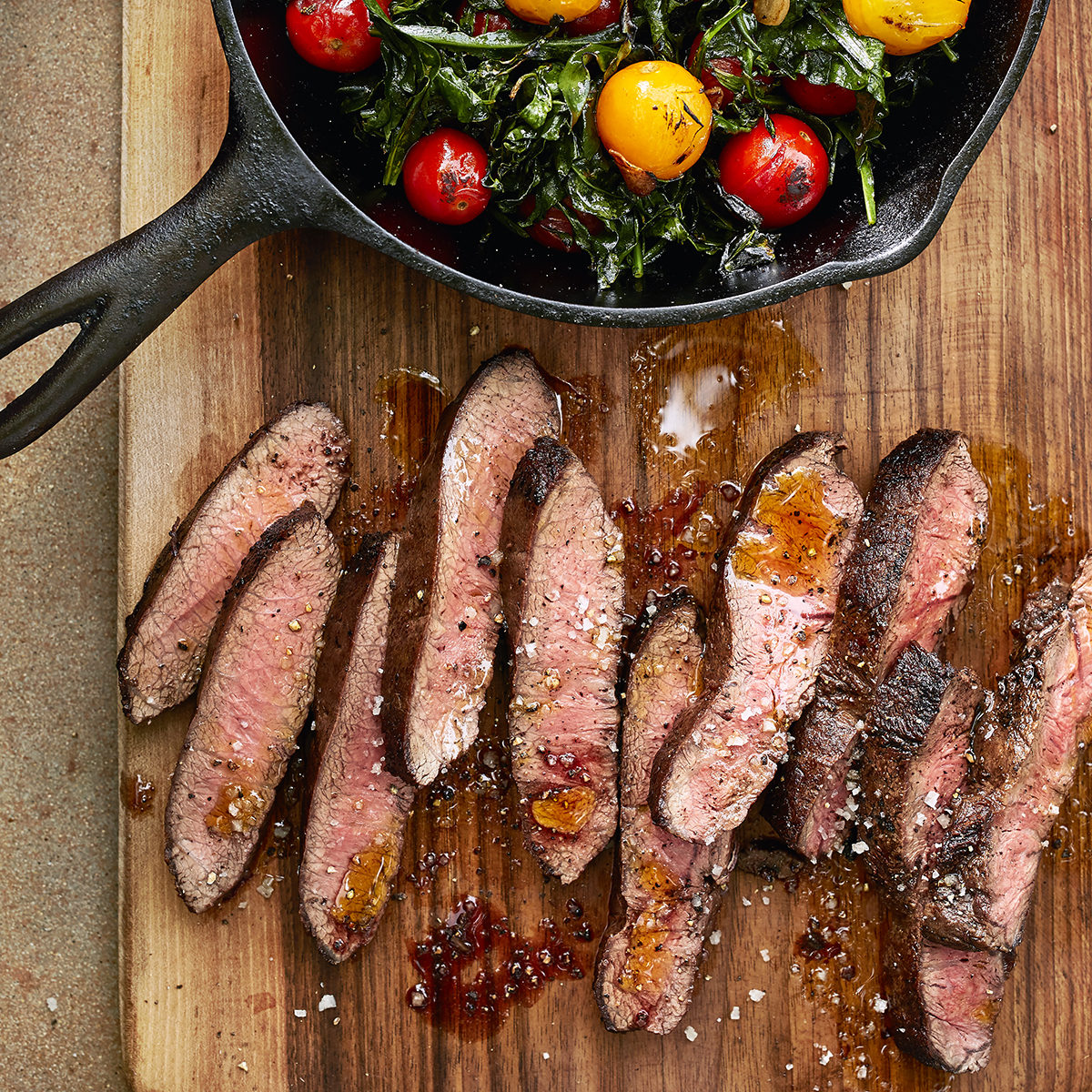 Seared Flat Iron Steak with Spigarello & Cherry Tomatoes on a skillet and a cutting board
